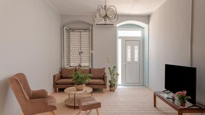 A living room with a sofa, two chairs, a coffee table, a TV on a wooden stand, and a door with a decorative glass panel. - Magganos House II Kefalonia (Kefalonia)