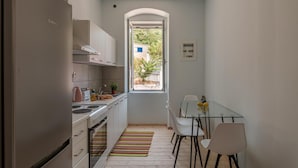 A compact kitchen with a Bosch refrigerator, a stove, and a dining area with a glass table and chairs. - Magganos House II Kefalonia (Kefalonia)