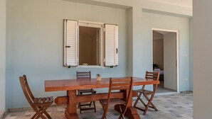 A dining area with a wooden table and chairs, a window with shutters, and a tiled floor. - Magganos House Kefalonia (Kefalonia)