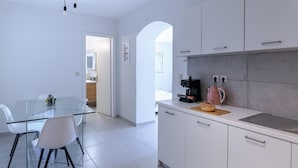 A modern kitchen with white cabinets, a glass dining table, and a coffee machine. - Magganos House Kefalonia (Kefalonia)
