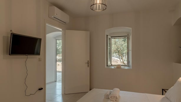 A bedroom with a bed, a TV, an air conditioner, a window, and a door leading to an outdoor area. - Magganos House Kefalonia (Kefalonia)