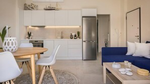 A modern kitchen with white cabinets, a stainless steel refrigerator, and a dining area with a wooden table and white chairs. - Casa Simone Kefalonia (Kefalonia)