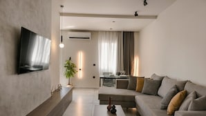 Een moderne woonkamer met een flatscreen televisie aan de muur, een bank, een salontafel en een eethoek op de achtergrond.