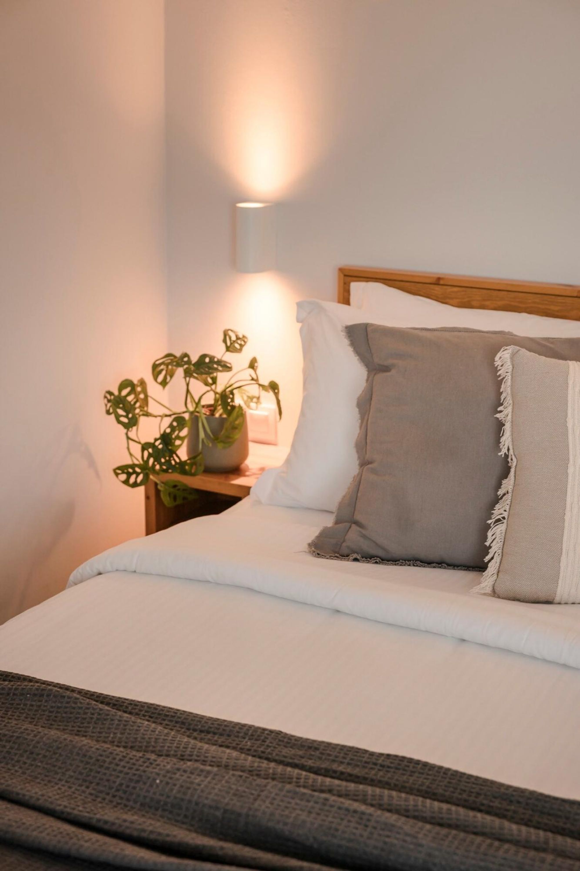 Un lit bien fait, avec des draps blancs, un oreiller gris et une tête de lit en bois.