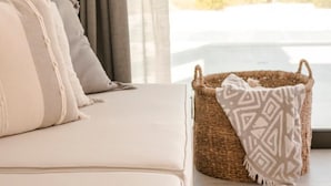 A modern living room with a sofa, cushions, and a woven basket with a patterned throw. - Nirvana - Unalome Villas (Kefalonia)