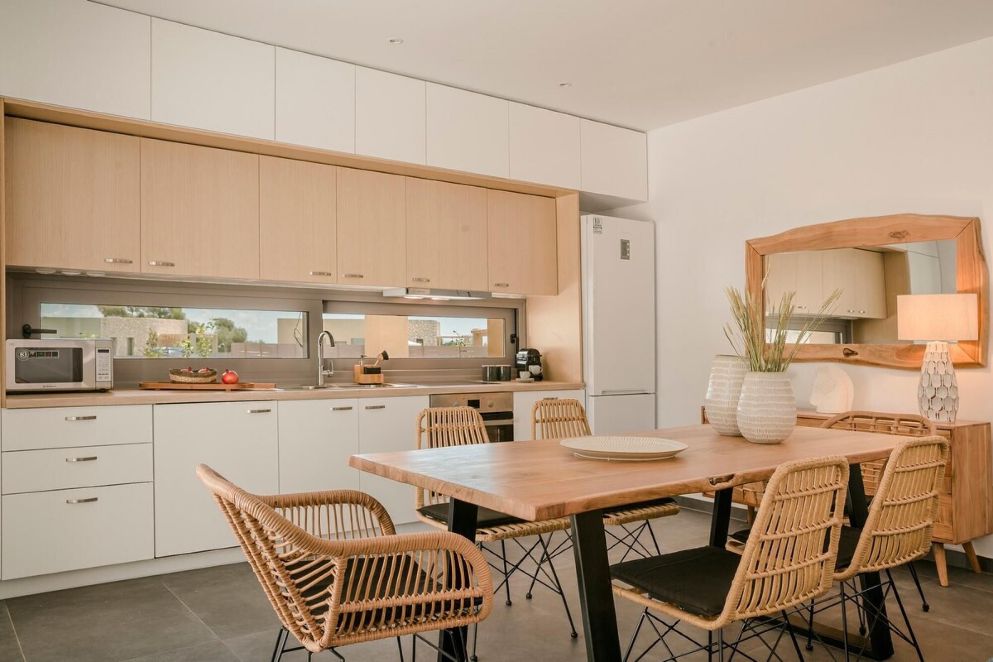 A modern kitchen with light wood cabinets, a stainless steel sink, and a dining area with wicker chairs and a wooden table.