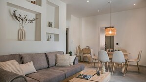 A modern living room with a grey sofa, a wooden coffee table, and a dining area with a round table and chairs.