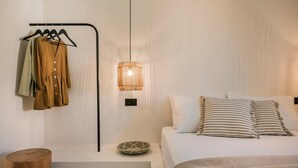 A bedroom with a bed, a hanging light fixture, a wooden stool, and a clothing rack with clothes.