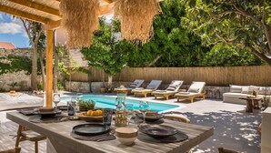An outdoor dining area with a pool, lounge chairs, and a pergola.