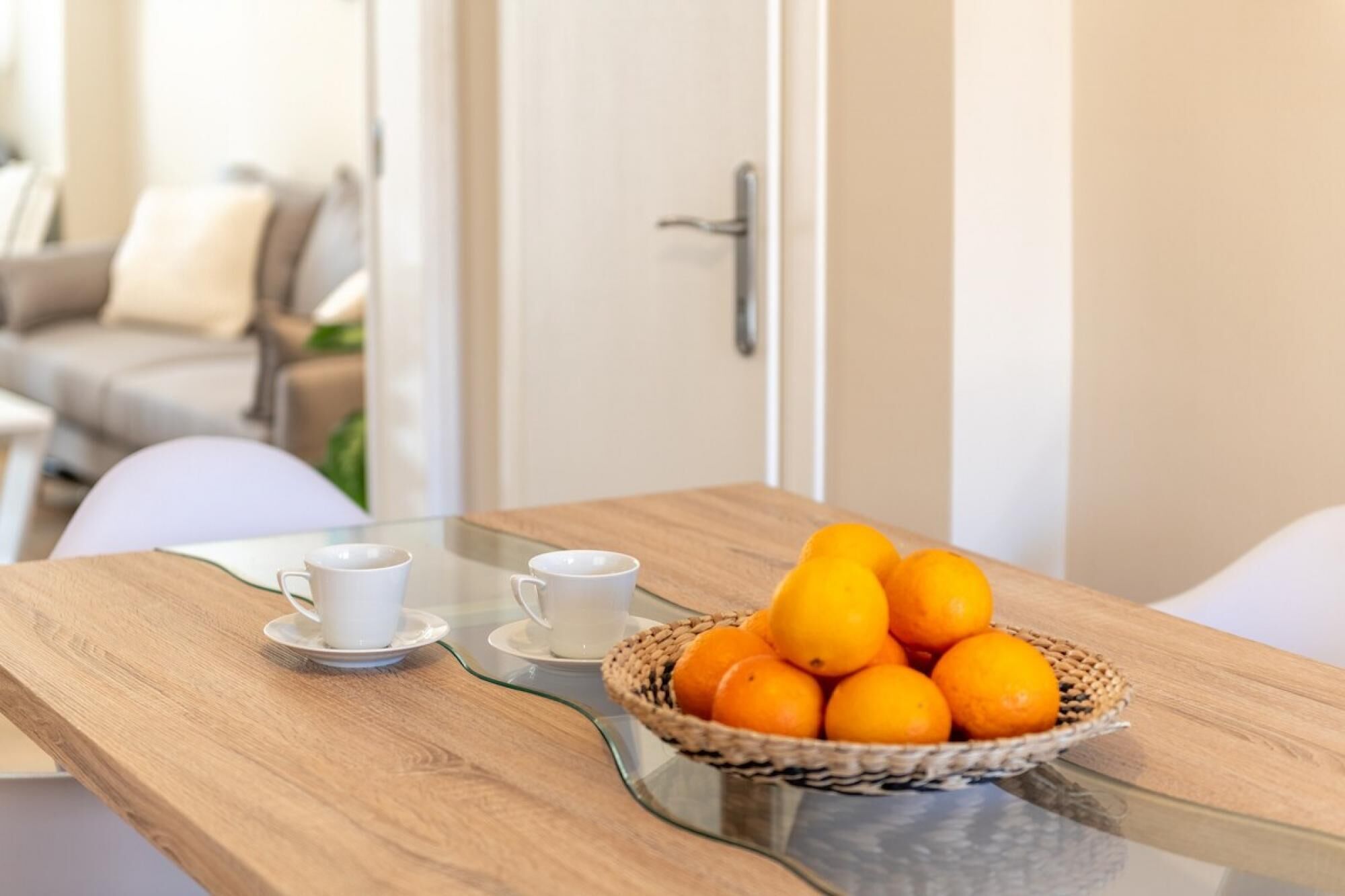 Una mesa de madera con dos tazas blancas y una cesta de naranjas.