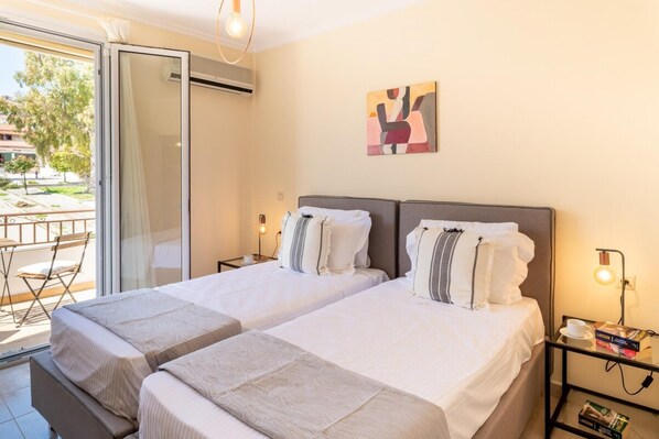 Habitación doble con dos camas, una puerta de vidrio que da a un espacio exterior y un cuadro en la pared.