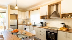 A modern kitchen with a glass-top dining table, a built-in oven, and a stainless steel range hood. - Entheos City Center Kefalonia (Kefalonia)