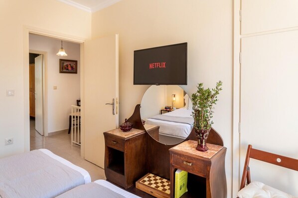 Habitación de hotel con dos camas, un televisor montado en la pared, un espejo, una mesita de madera y una planta en maceta.