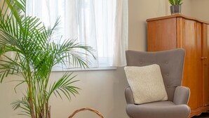A room with a grey armchair, a potted plant, a wooden cabinet, and a window with sheer curtains. - Entheos City Center Kefalonia (Kefalonia)
