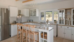 Une cuisine moderne avec des meubles blancs, un réfrigérateur en acier inoxydable, des tabourets en bois et un grand îlot central.