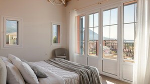 Une chambre à coucher avec un lit, une chaise et de grandes fenêtres donnant sur des immeubles et des montagnes.