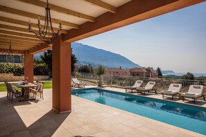Zona de piscina con sillones de descanso, una mesa y vistas a montañas.
