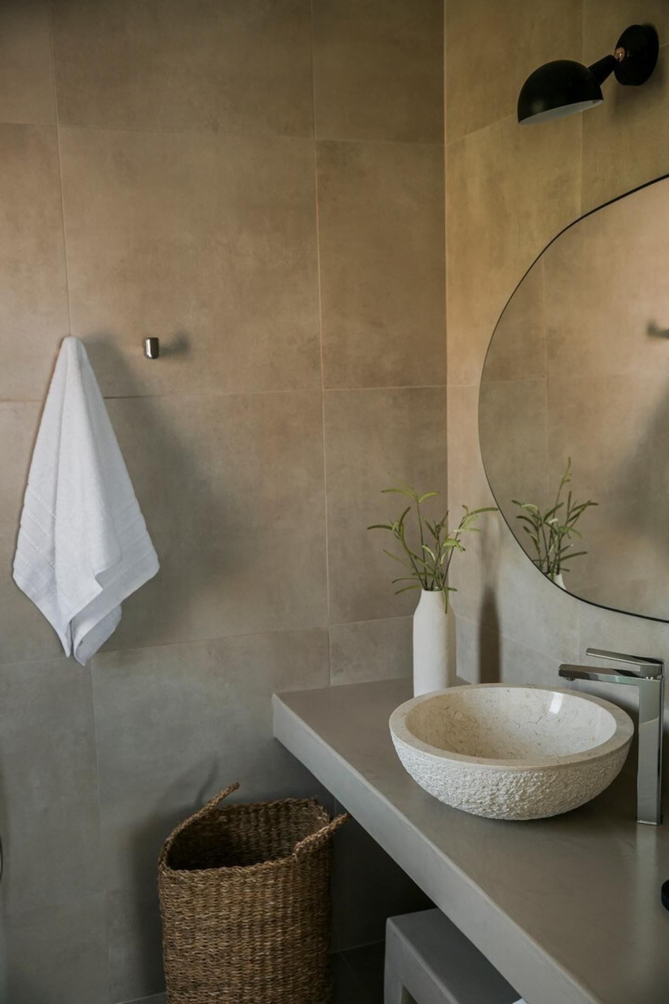 Une salle de bain moderne avec un grand miroir, un lavabo rond et une serviette suspendue à un porte-serviettes fixé au mur.