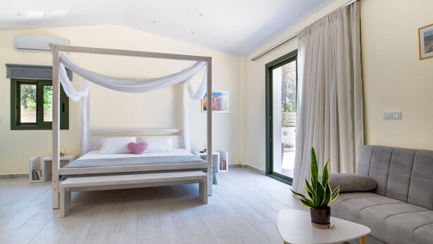 A modern bedroom with a canopy bed, a sofa, a small table, and a potted plant. - Arktos Sunset Villa (Kefalonia)