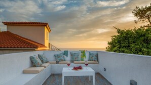 A rooftop terrace with a seating area, a table with a fruit bowl and glasses, and a view of the sunset. - Arktos Sunset Villa (Kefalonia)