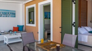A modern outdoor seating area with a glass-top table, chairs, and a small white table. - Arktos Sunset Villa (Kefalonia)