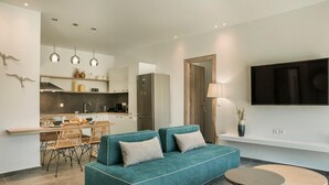 Un salon moderne avec un canapé de couleur turquoise, une petite table ronde et un coin cuisine à l’arrière-plan.
