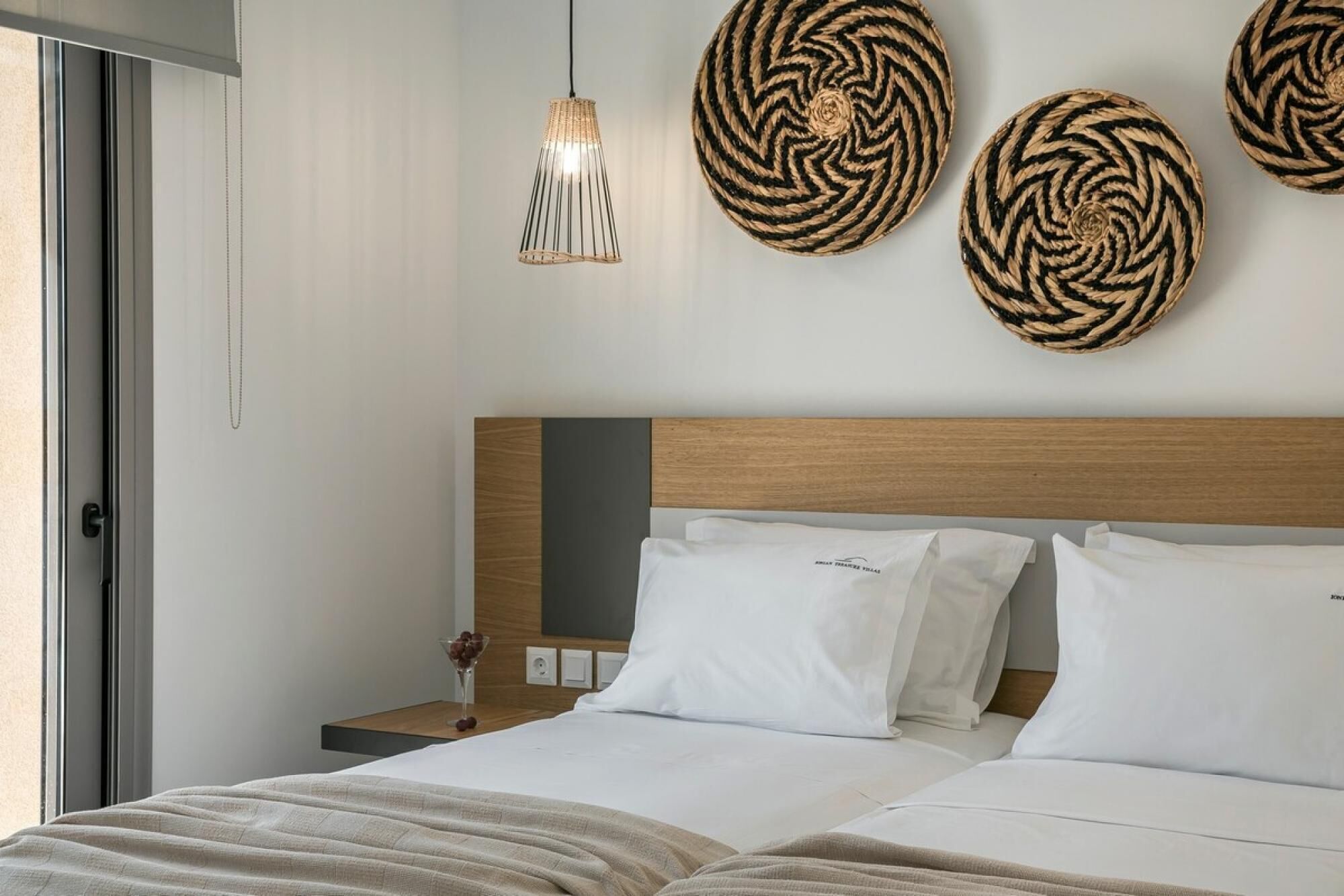 A modern hotel room with a wooden headboard, white bedding, and three woven wall art pieces.
