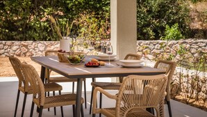 Un espace extérieur aménagé pour les repas, avec une table dressée pour quatre personnes, entourée de chaises en osier.