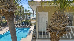 A poolside view with a clear blue pool, palm trees, and a building with a white door marked '212'. - Caribbean Dunes by Panhandle Getaways (Destin)
