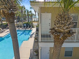 A poolside view with a clear blue pool, palm trees, and a building with a white door marked '212'.