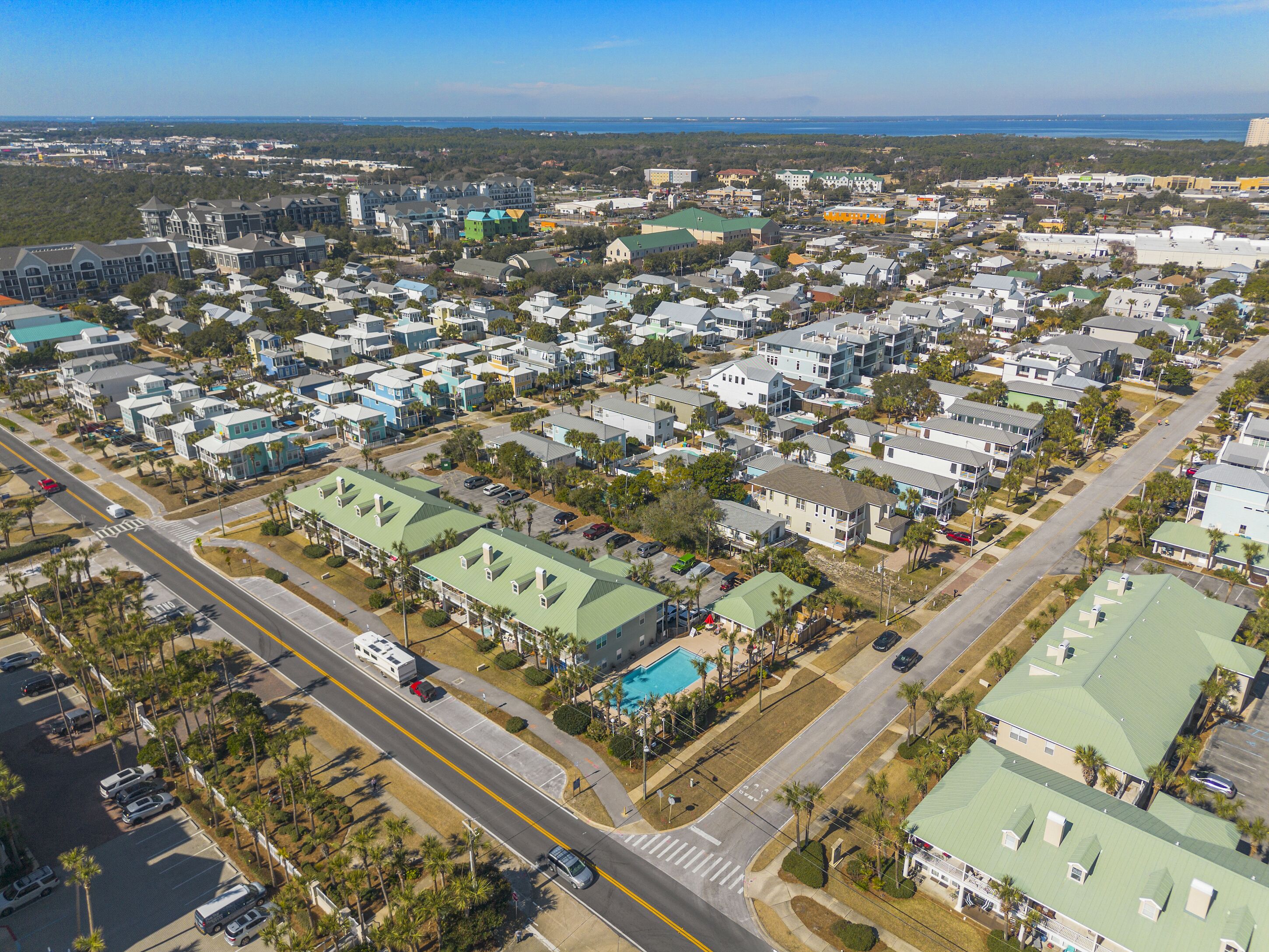 An aerial view of a residential area with multiple houses, roads, and a large green-roofed building with a swimming pool.