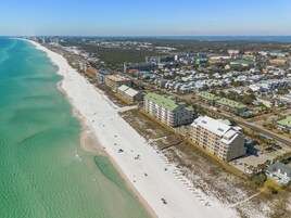 An aerial view of a coastal area with a beach, buildings, and a road.