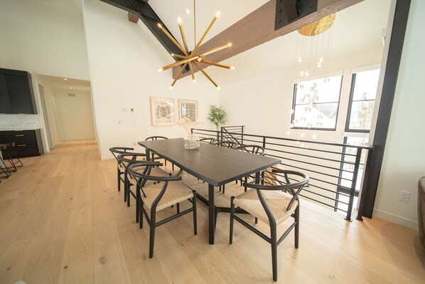 A dining area with a dark wooden table and black metal chairs, a modern chandelier, and a view of the outdoors through large windows. - Luxury Home • Pvt Hot Tub • Pool • Shuttle (Keystone)