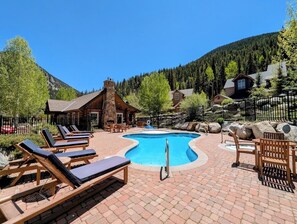 A pool area with lounge chairs, a pool, and a stone building in a mountainous setting.