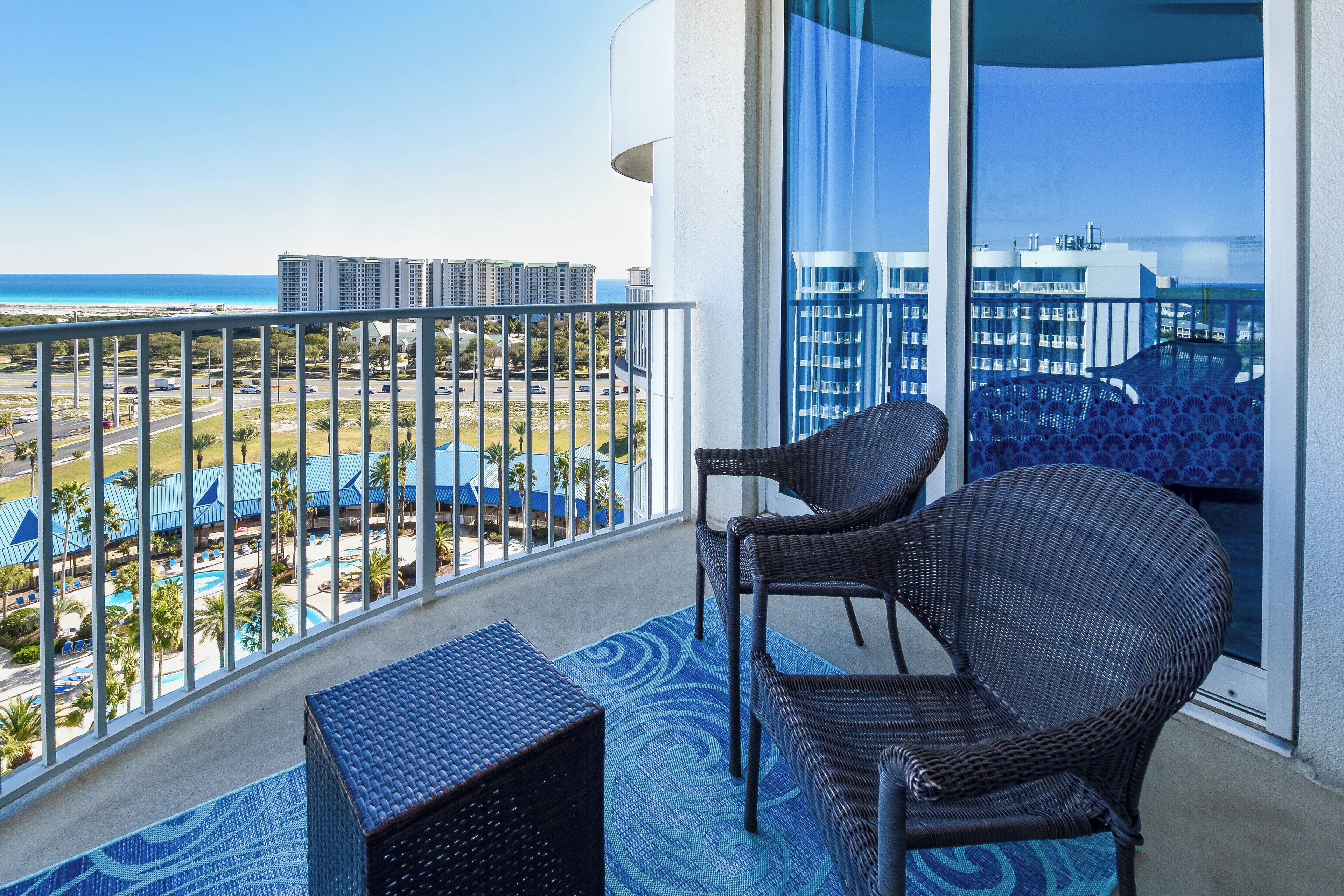 A balcony with wicker furniture, a view of a beach, and a pool area.