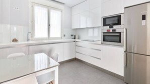 Una cocina moderna con armarios blancos, horno empotrado, microondas y refrigerador.