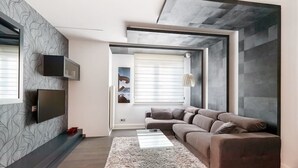 Una sala de estar moderna con una pared gris estampada, un sofá gris, una mesa de centro de vidrio y un ventanal con persianas.