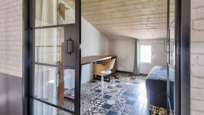 Ein Zimmer mit Holzbalkendecke, einem Schreibtisch mit Stuhl, einem Bett und einem fußbodenreifen Muster.