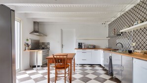 Eine Küche mit Schachbrettmuster-Boden, weißen Schränken, einem Holztisch und einem Edelstahl-Kühlschrank.