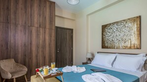 Habitación de hotel con cama, una silla, mesita de noche con lámpara, un cuadro en la pared y una bandeja con toallas y un vaso de zumo de naranja.