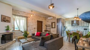 Una sala de estar con sofá, mesa de centro y chimenea. Se observa un comedor con sillas y una mesa. La cocina es visible, con estufa y alacenas.