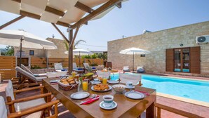 Un área de comedor al aire libre con piscina, mobiliario de madera y sombrillas.