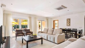 A modern living room with a sofa, armchairs, a coffee table, and a TV. There is a dining area with a table and chairs. - Villa Cabrita de Parra (Vale Rebelho)