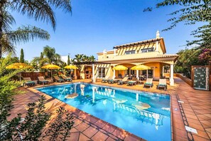 Zona junto a la piscina con piscina, tumbonas y sombrillas.