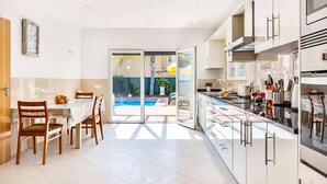 A modern kitchen with a dining area, a pool view, and a sliding glass door leading to the outdoor area. - Villa Cabrita de Parra (Vale Rebelho)
