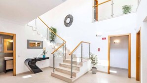 A modern interior with a curved reception desk, a staircase with glass railings, and a large wall clock. - Villa Cabrita de Parra (Vale Rebelho)