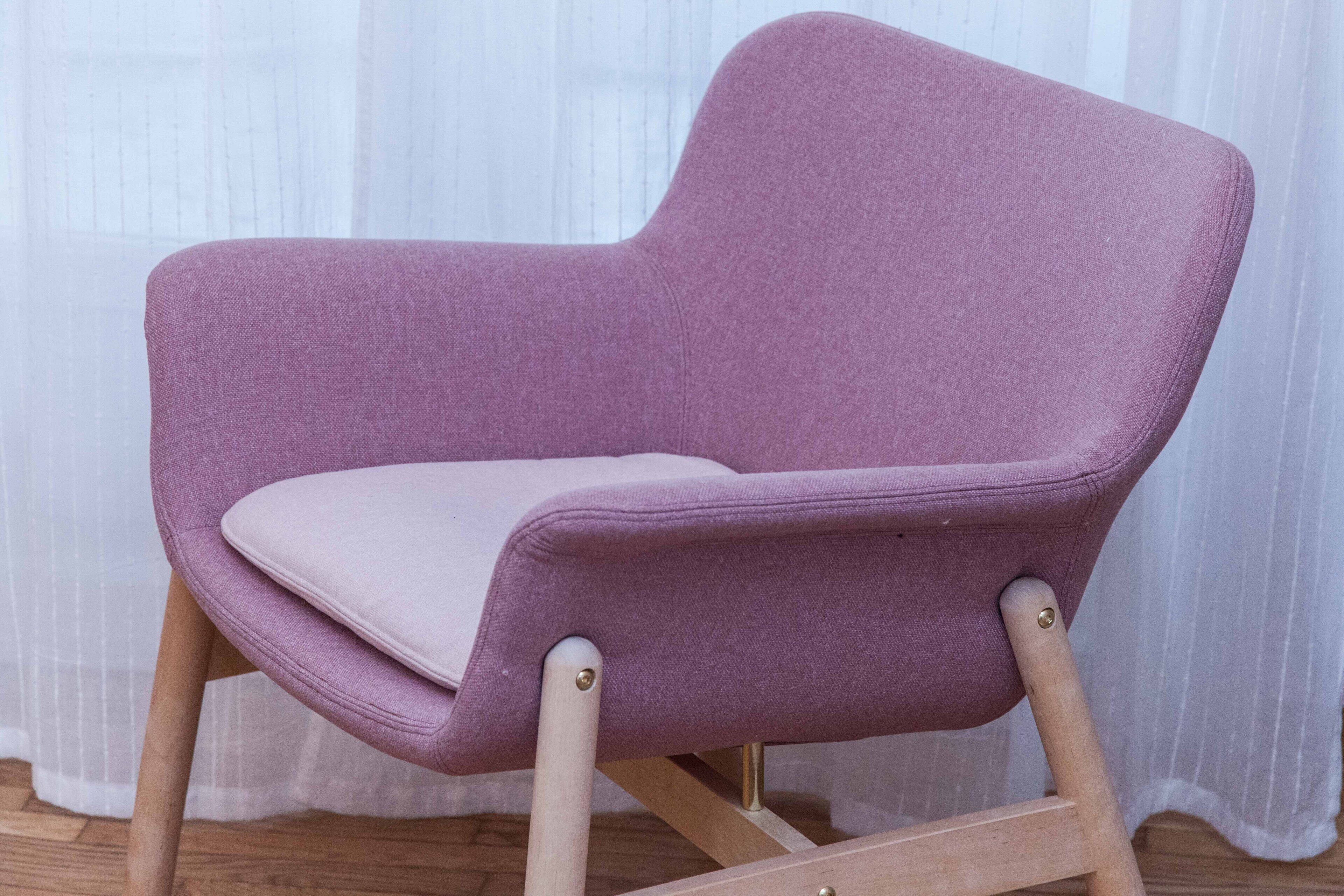 Un fauteuil violet avec des pieds en bois et un coussin.
