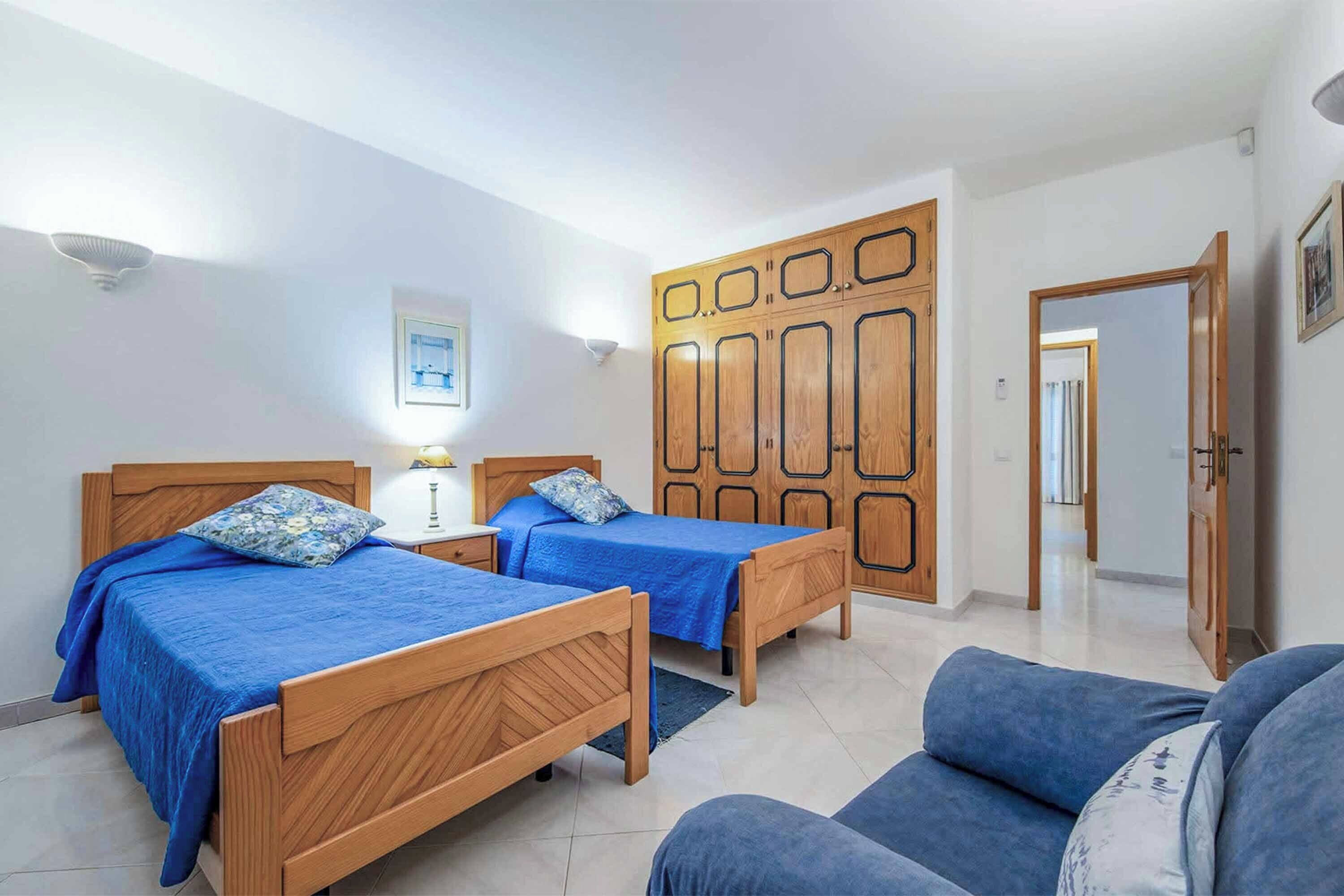 A room with two wooden beds, a sofa, and a wardrobe with geometric patterns.