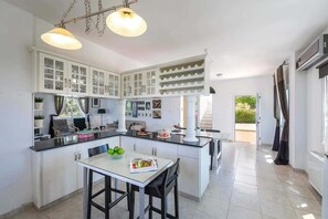 A modern kitchen with white cabinets, a dining area with a table and chairs, and pendant lighting. - Pine Retreat - Four Bedroom Villa, Sleeps 8 (Argaka)