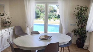 Un coin repas avec une table ronde et des chaises, une plante en pot, et une vue sur une piscine et la verdure environnante.